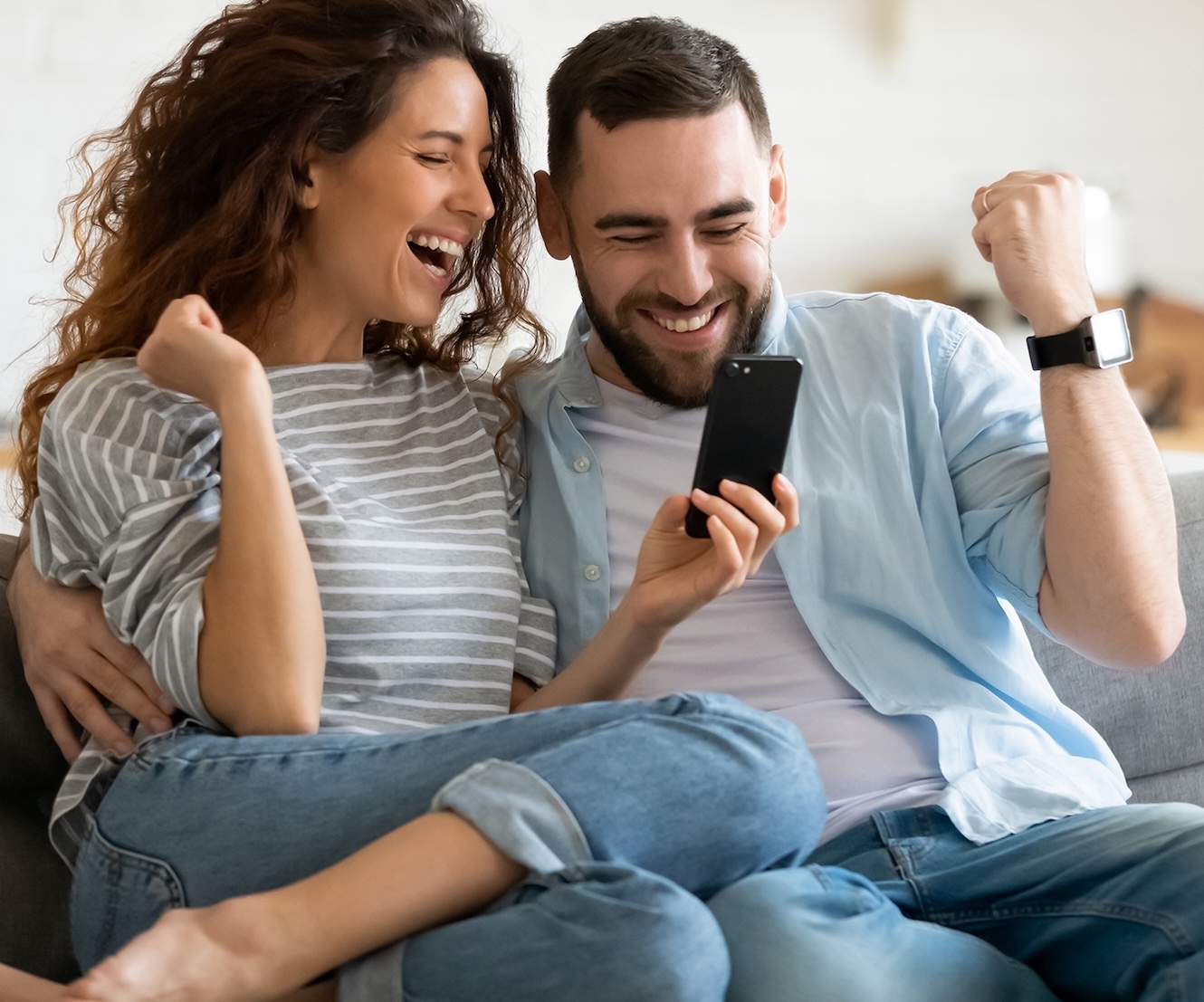 Excited,Overjoyed,Couple,Resting,On,Couch,Holding,Smart,Phone,Celebrating